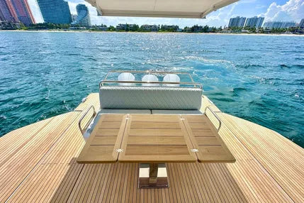 Yacht deck with wooden flooring and table on a body of water with buildings in the background